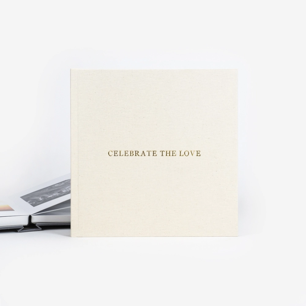 Elegant cream-colored square card with gold foil text reading CELEBRATE THE LOVE, leaning against a white background.