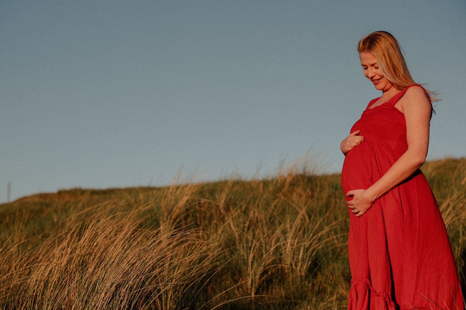 Zwangere vrouw in rode jurk in de duinen, documentaire zwangerschapsfotografie Leiden en Den Haag door Mama Nora Fotografie
