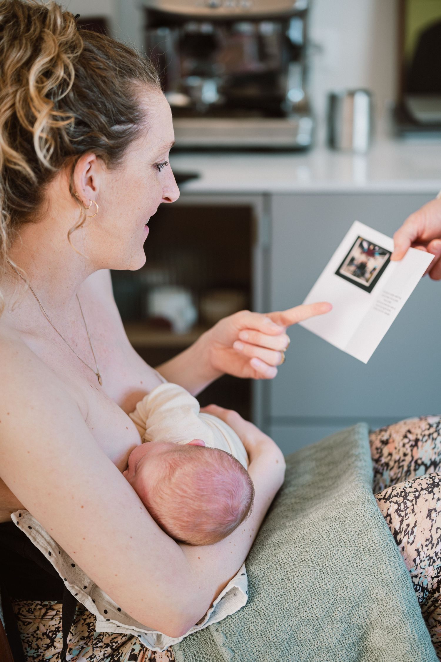 Moeder geeft borstvoeding en leest felicitatiekaartje, kraamtijdfotograaf Den Haag