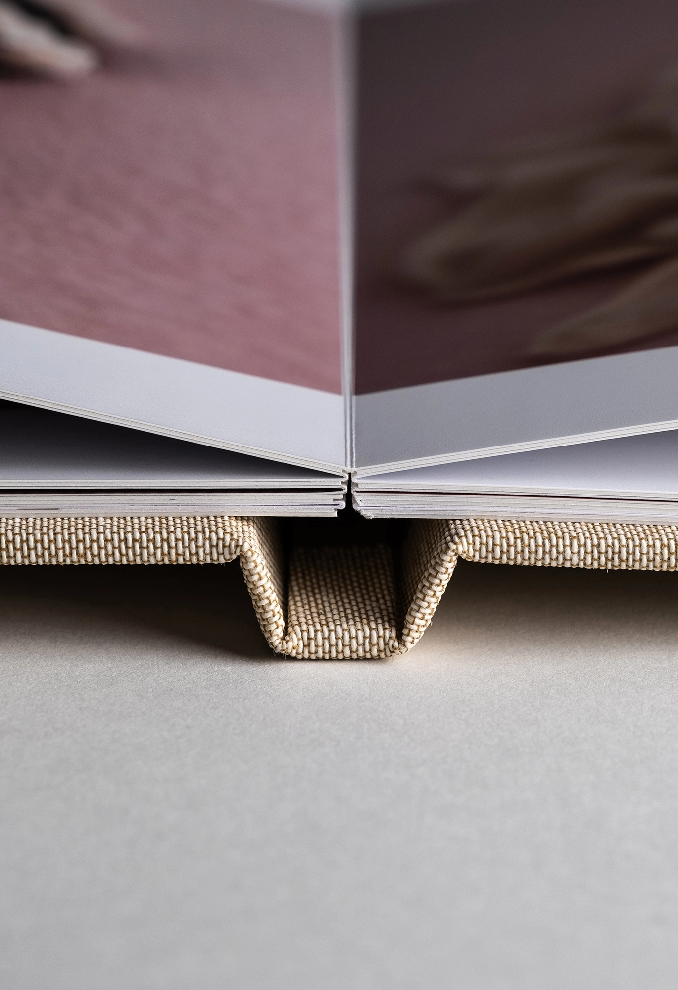 Close-up of an open photo book with linen fabric cover, showing layflat binding and glossy pages on gray background.