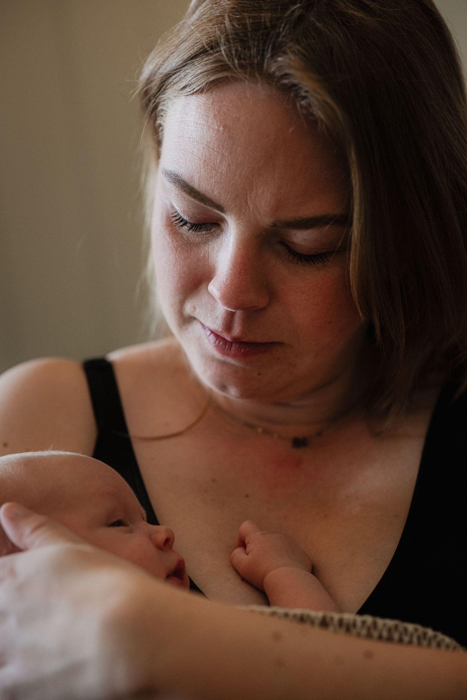A mother gazes lovingly at her newborn baby cradled in her arms, wearing a black top.