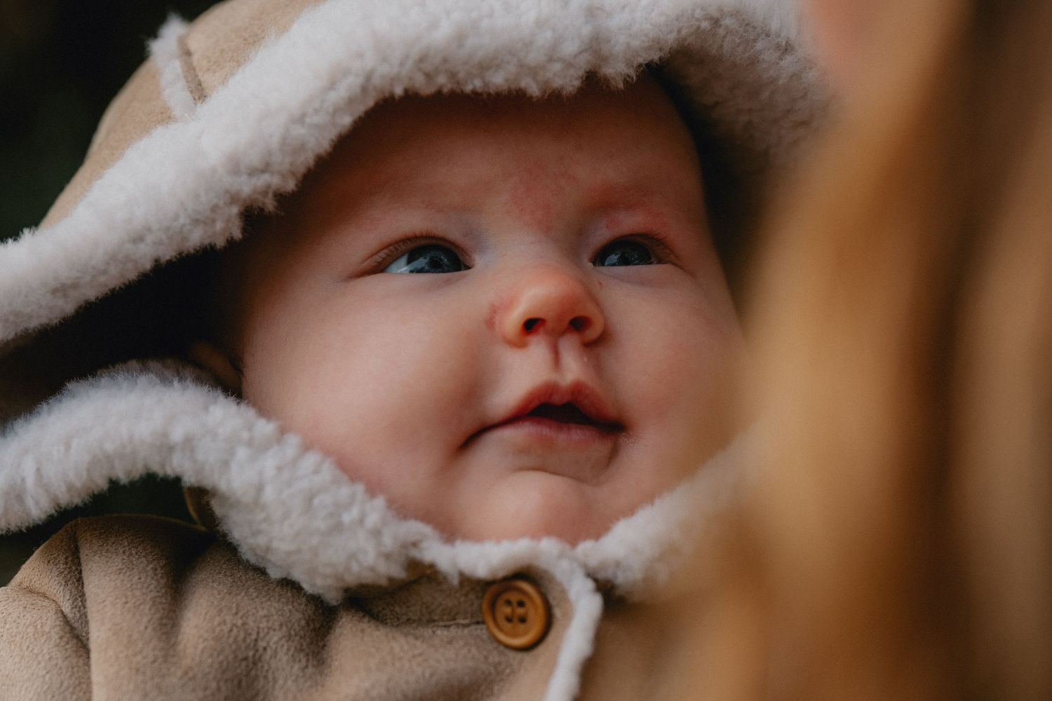 A baby wearing a cozy white winter hat smiles warmly at the camera.
