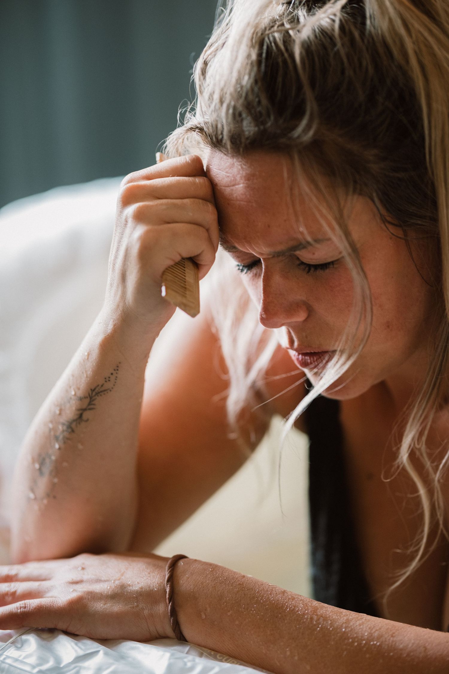 A distressed woman with blonde hair rests her head on her fist, looking down with a sad expression.