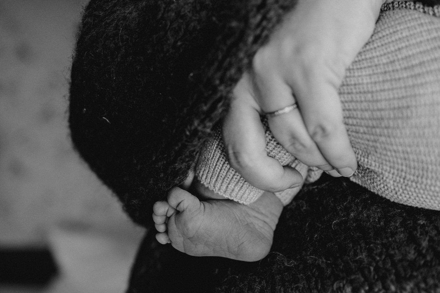 Black and white photo of adult hands gently holding a newborn baby's tiny feet.