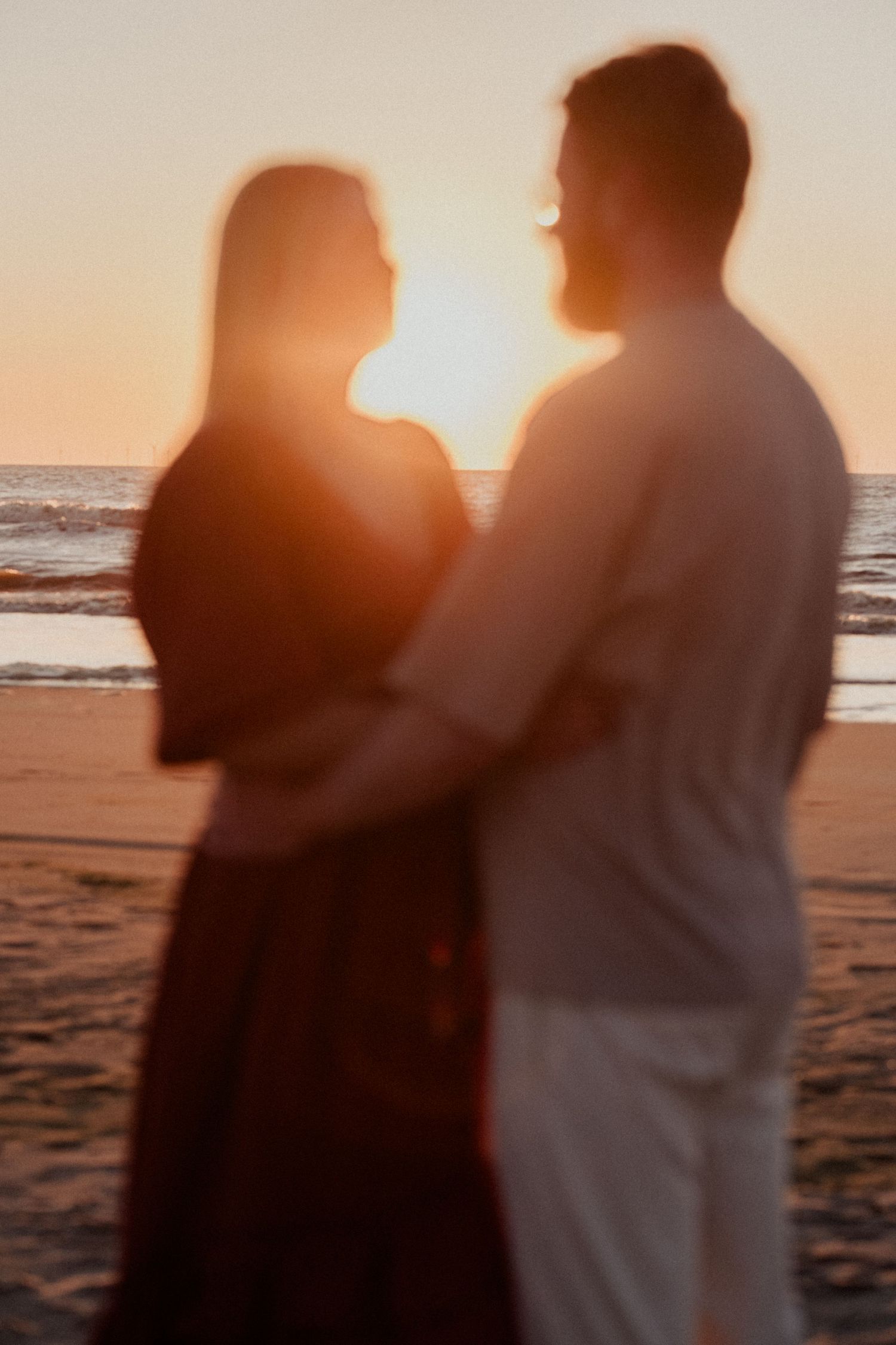 Blurred silhouette of a romantic couple embracing on a beach at golden sunset with ocean waves behind them.