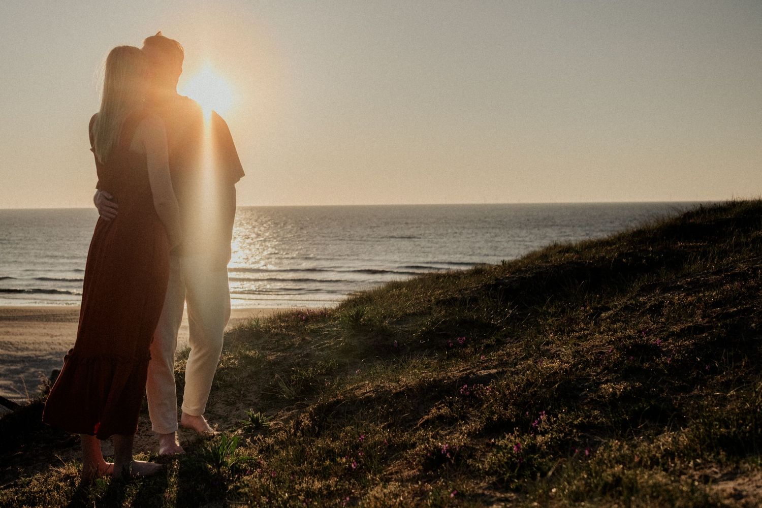 Couple silhouetted against golden sunset on a coastal cliff overlooking the ocean, sharing a romantic embrace.