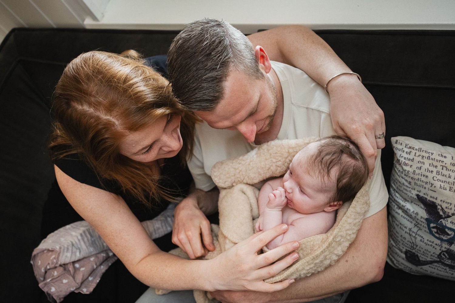Parents lovingly gazing at their sleeping newborn baby wrapped in a cozy knit blanket.