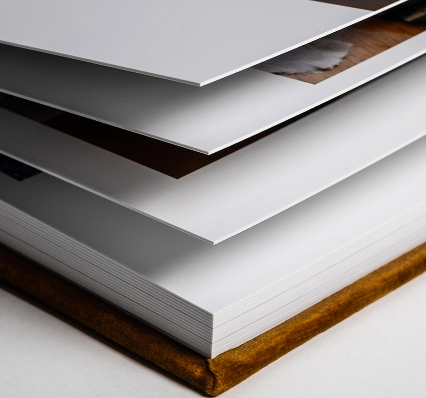 Stack of thick white photo paper sheets with a brown leather-bound book base, showcasing premium print quality.