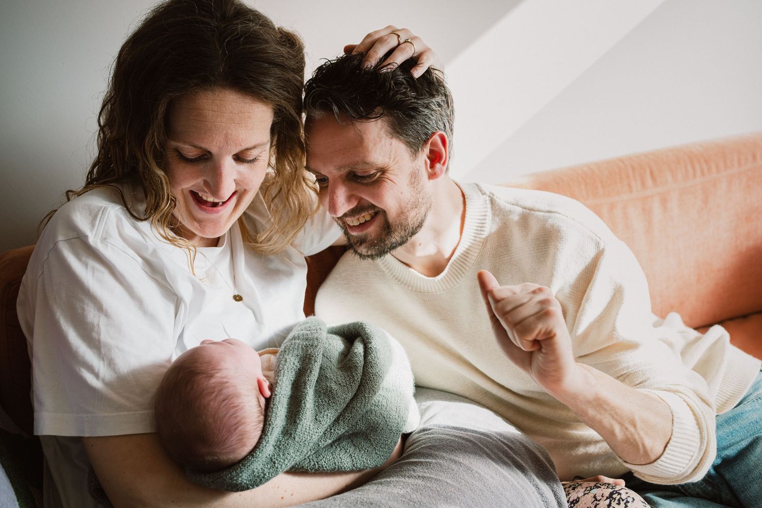 Happy parents smiling and bonding with their newborn baby wrapped in a teal blanket at home.