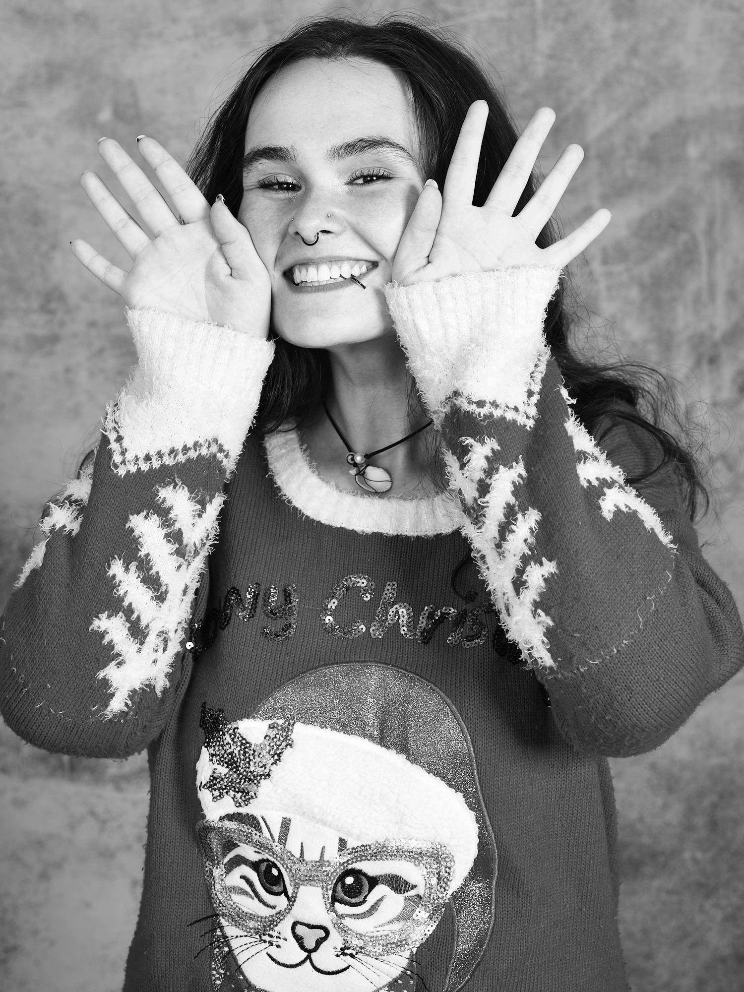 Person wearing a winter sweater with a cat design shows off white mittens while smiling.