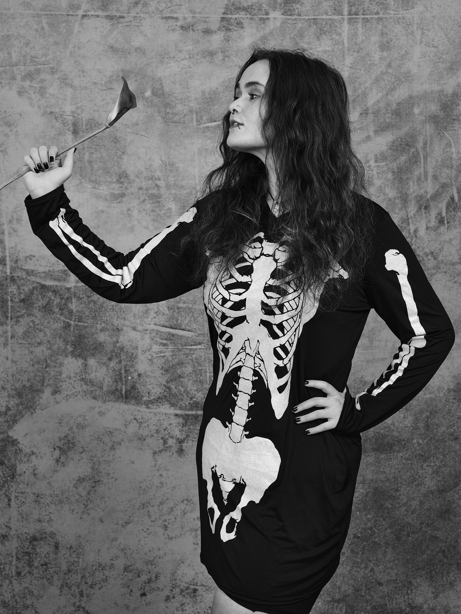Model poses in a black skeleton-print dress against a textured gray wall.