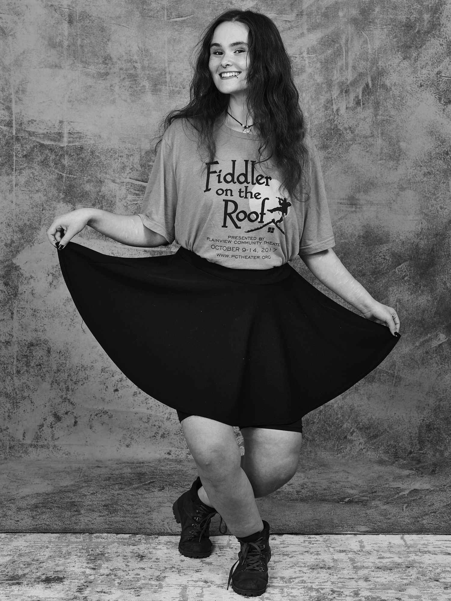 Person wearing a Fiddler on the Roof t-shirt poses playfully with a flared black skirt.