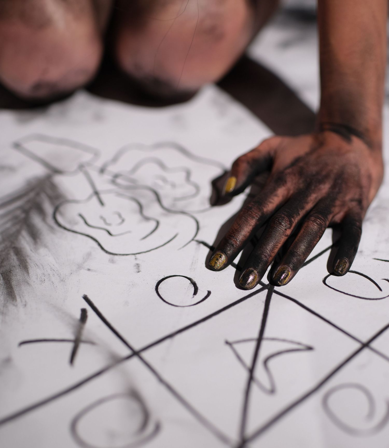 Close-up of hands drawing symbols and patterns with charcoal.