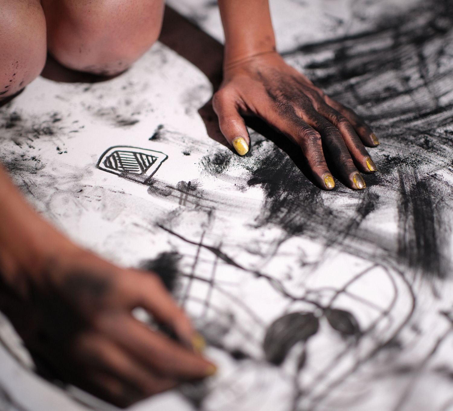 Close up of hands drawing with charcoal on white paper.