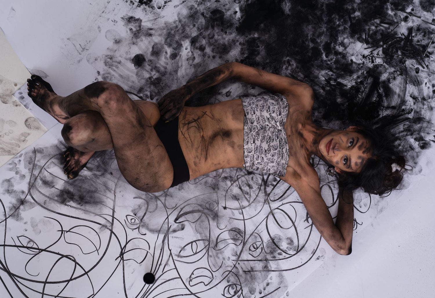 Artistic portrait of figure reclining on floor with charcoal drawings.