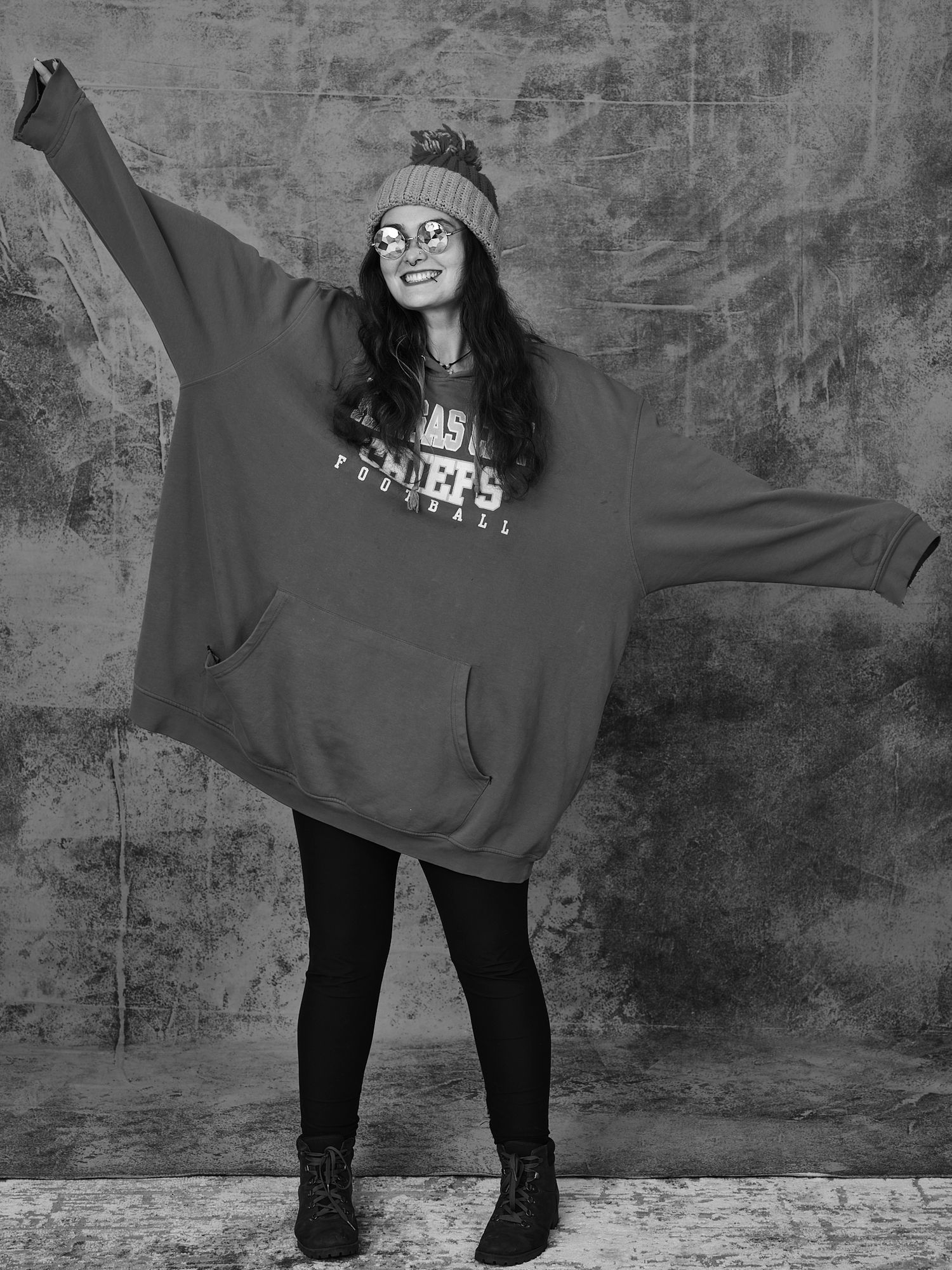 Person in oversized sweatshirt and leggings spreads arms wide in playful pose.
