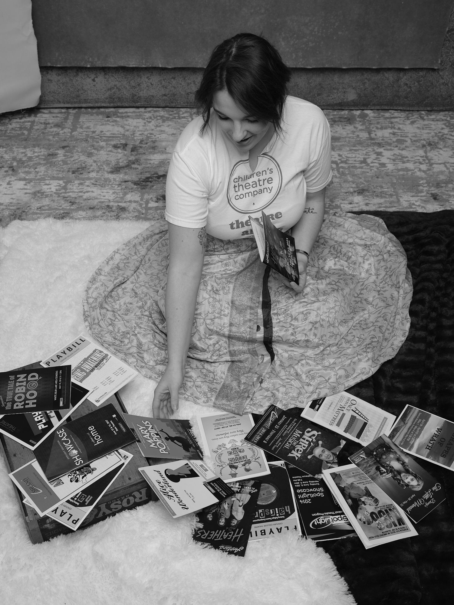 An overhead view of someone arranging books on the floor while wearing a graphic t-shirt.