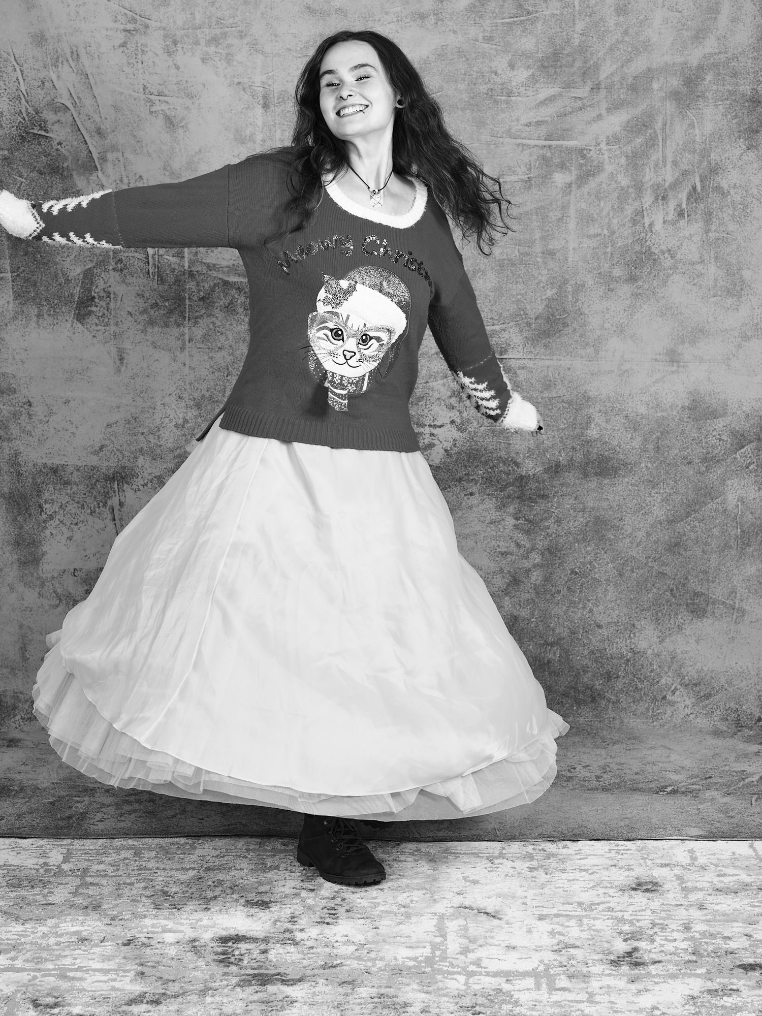 Dancer spins in a flowing white skirt and dark sweater against a gray studio backdrop.