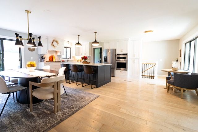 Open-concept kitchen and dining area with light hardwood floors, dark island, modern pendant lights, and white cabinetry.
