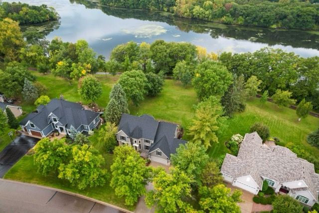 Aerial view of residential homes nestled among lush green trees beside a serene lake in a peaceful neighborhood.