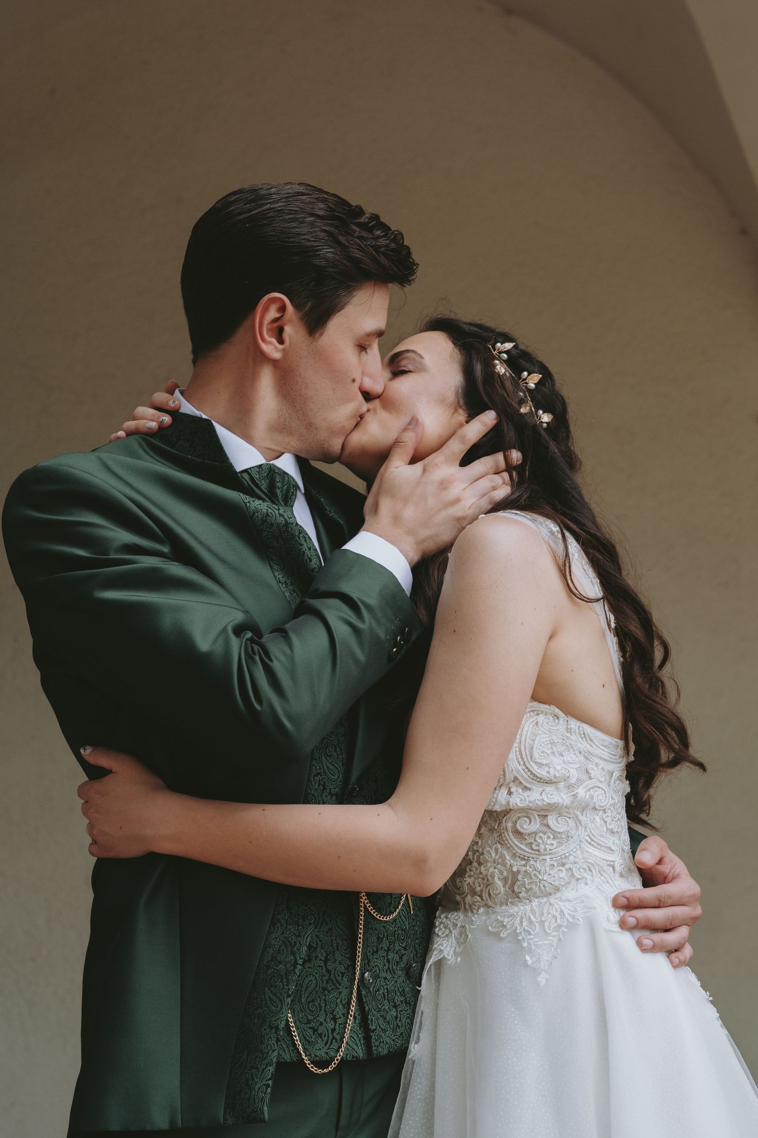 A romantic sequence of wedding photos showing a couple in green suit and white dress sharing tender kisses under an archway.