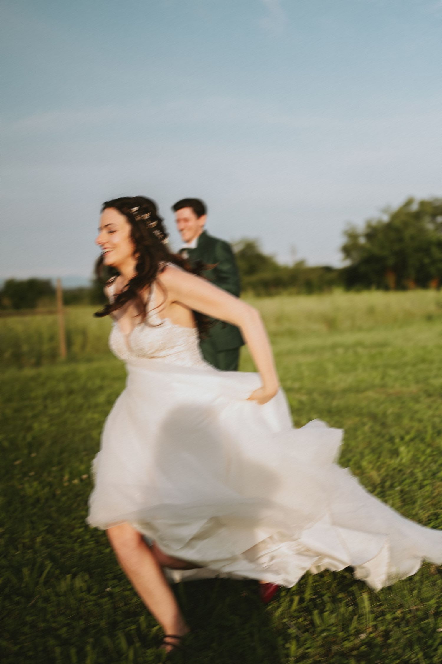 A bride and groom running through a grassy field on their wedding day.
