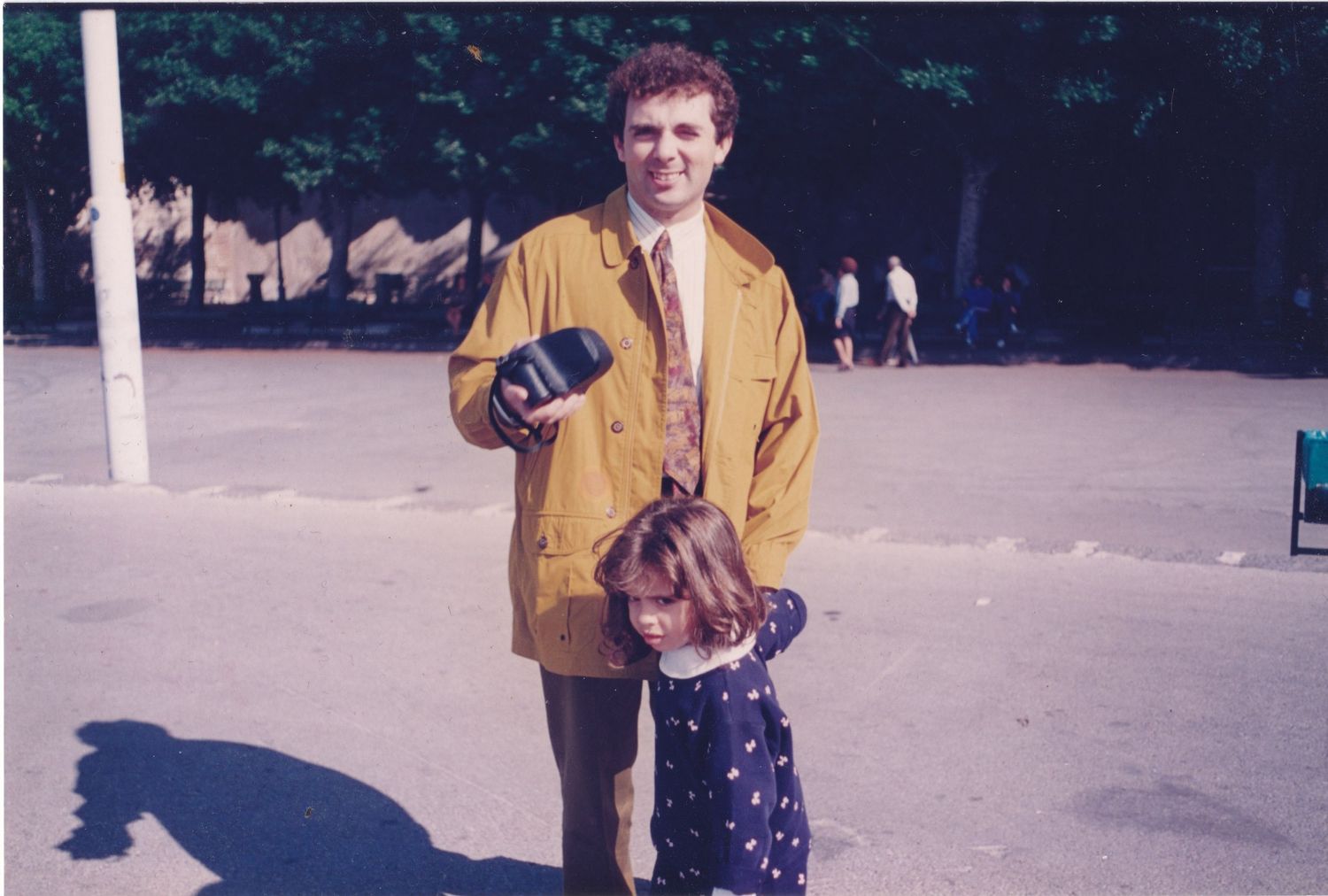 Person in yellow jacket standing outdoors on a bright day.