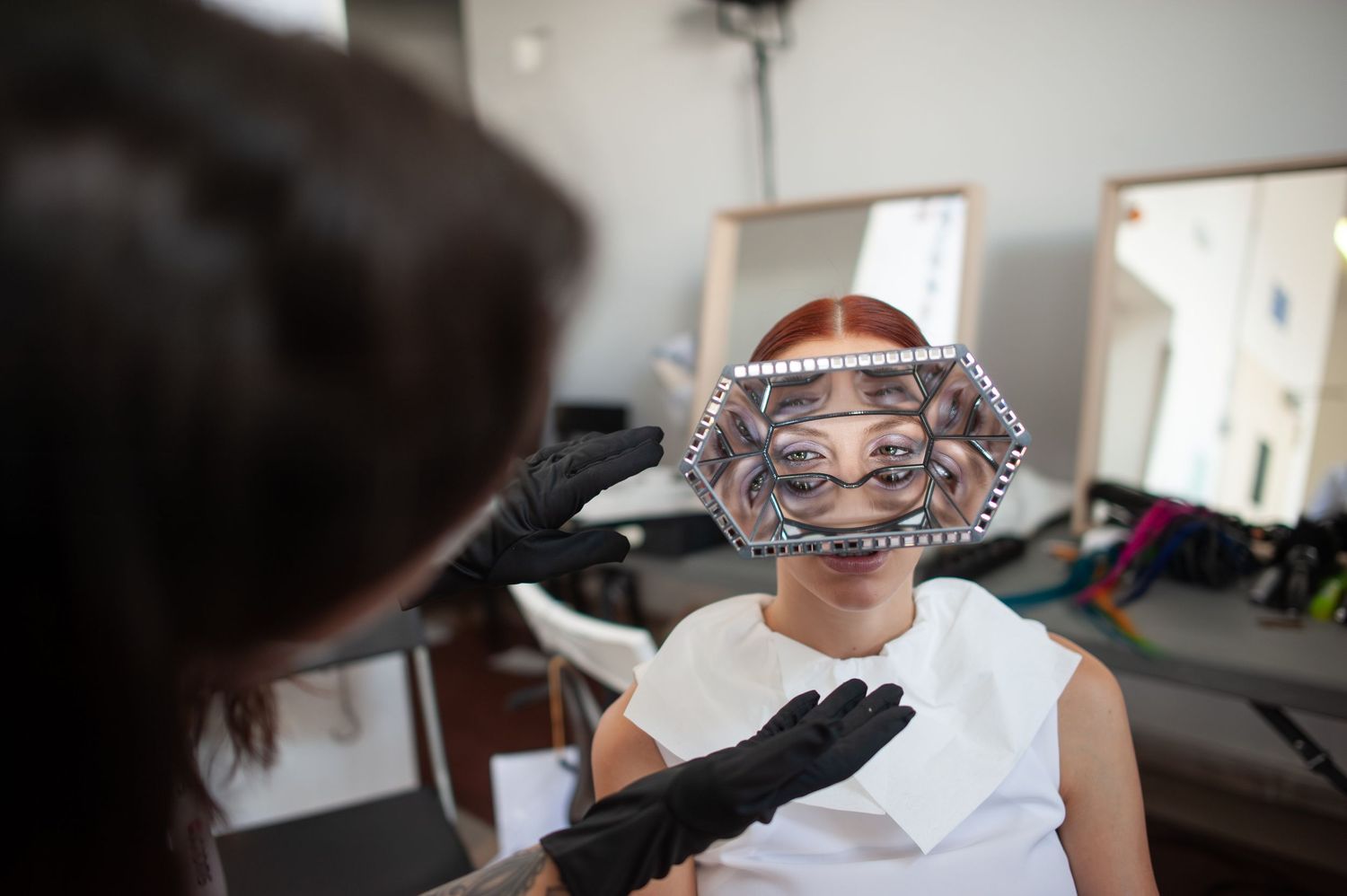 Esthetician applying a silver facial mask to a client in a modern beauty salon with mirrors in background.