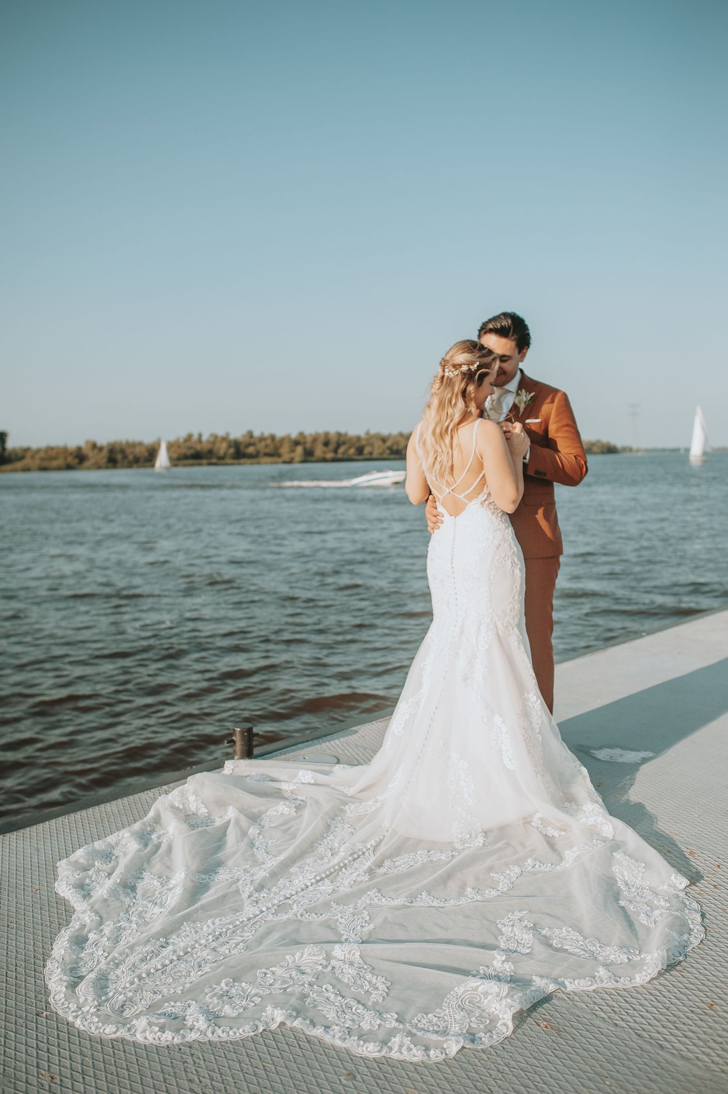 Waterfront wedding photo showing detailed lace train of bride's dress against ocean backdrop.