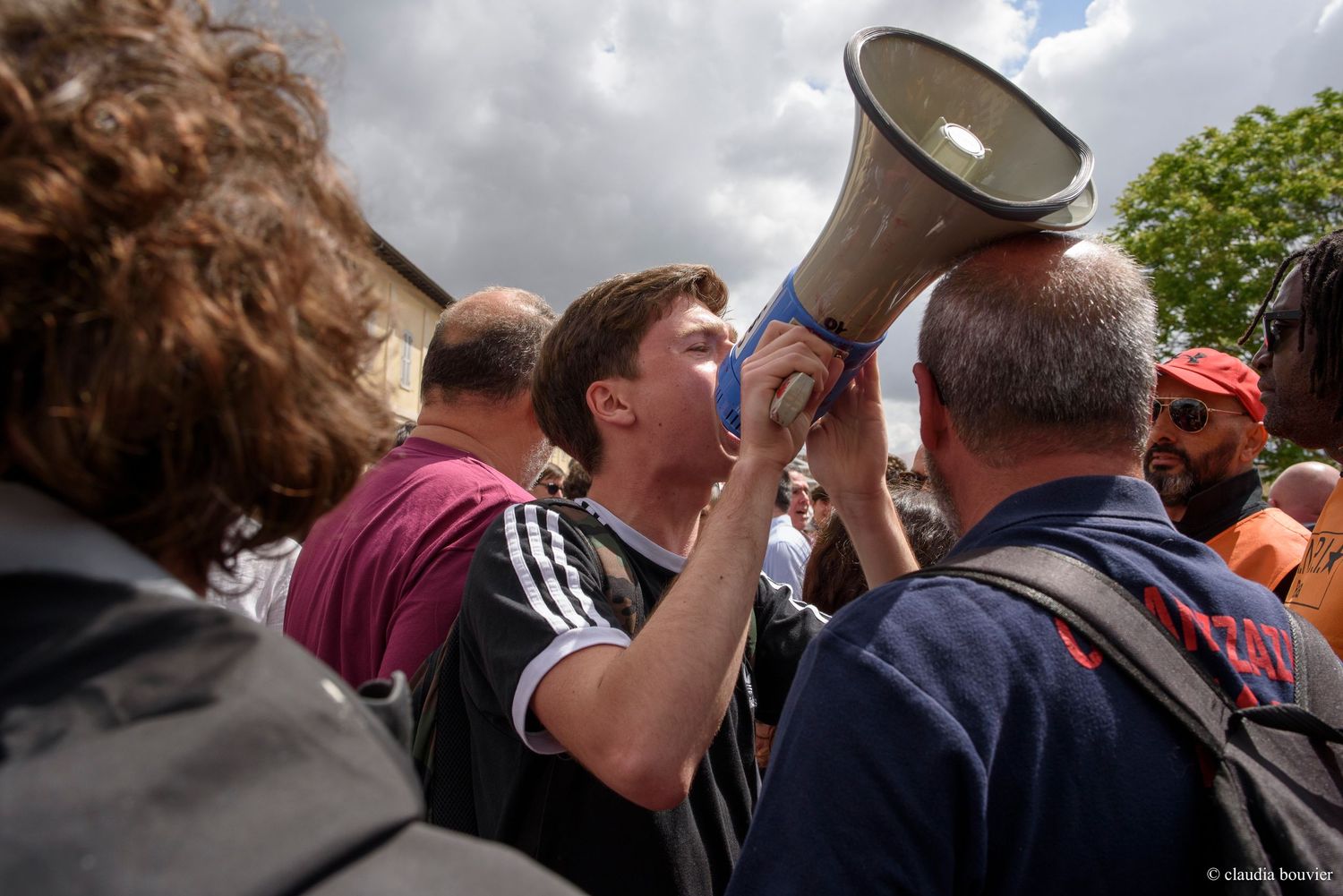 Activist using megaphone to address crowd at outdoor protest rally on cloudy day.