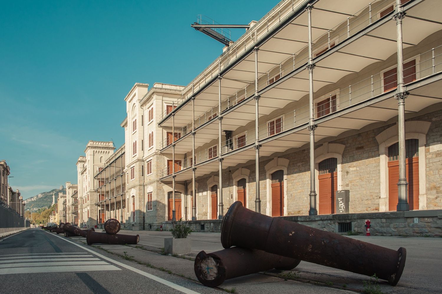 Historic building facade with rusty cannons displayed along a sunny street in a European coastal town.