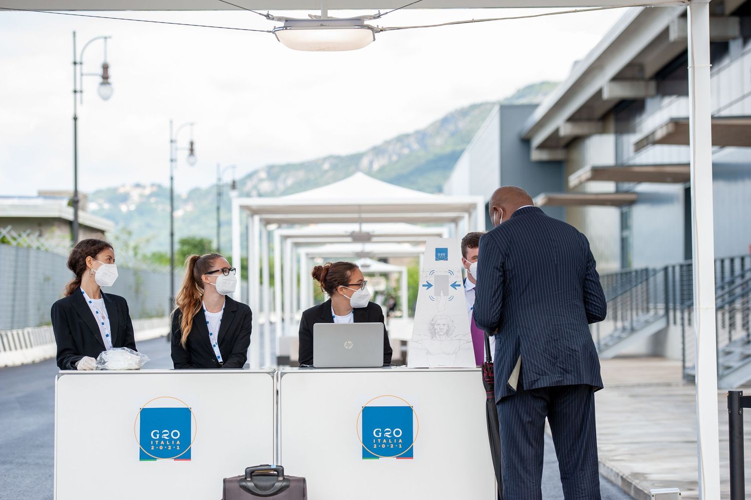 G20 registration desk with masked staff assisting a guest at an outdoor conference venue.