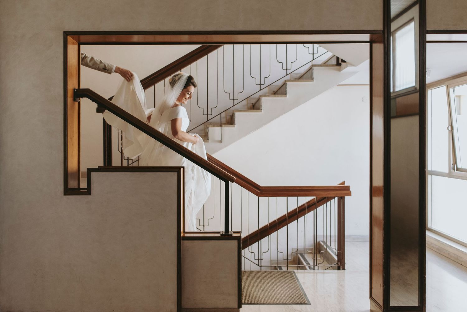 Modern wooden staircase with white walls and metal cable railing system illuminated by natural light.