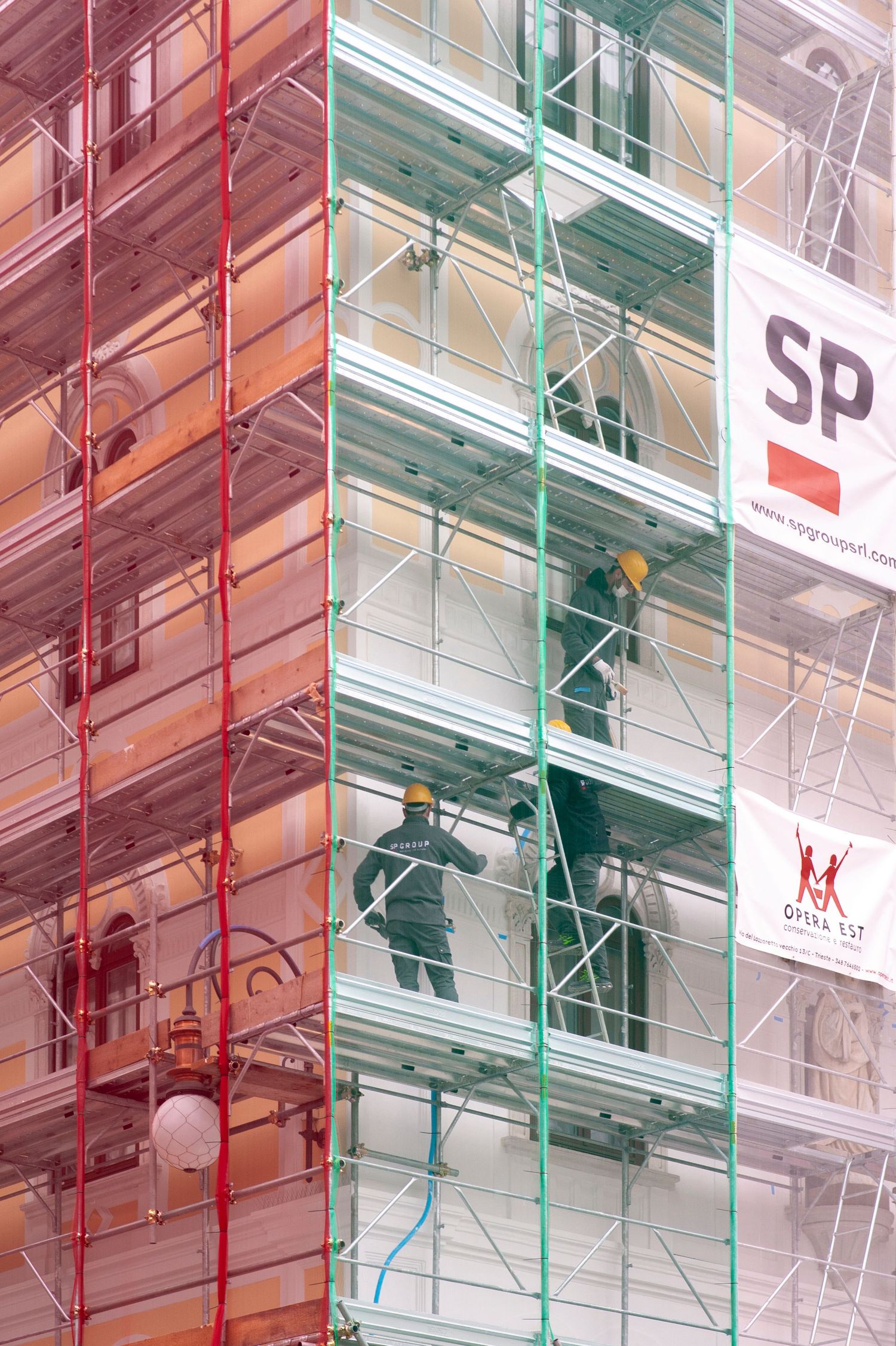 Construction workers in hard hats climbing scaffolding on a building facade during renovation work.