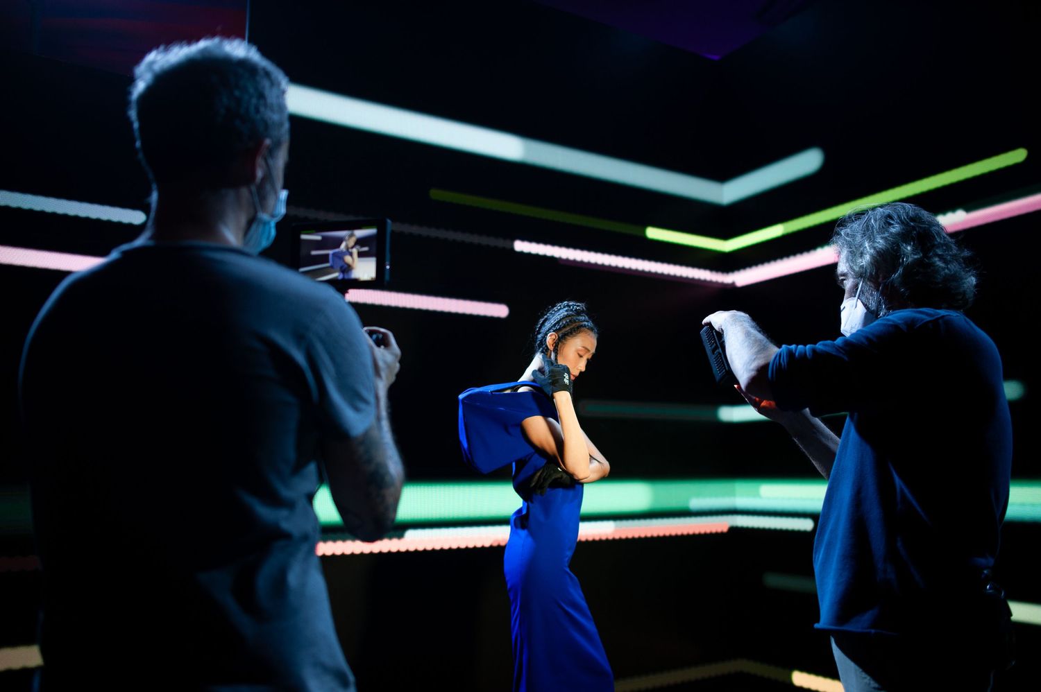 A woman in blue practices boxing in a neon-lit room while two people observe and film her training session.