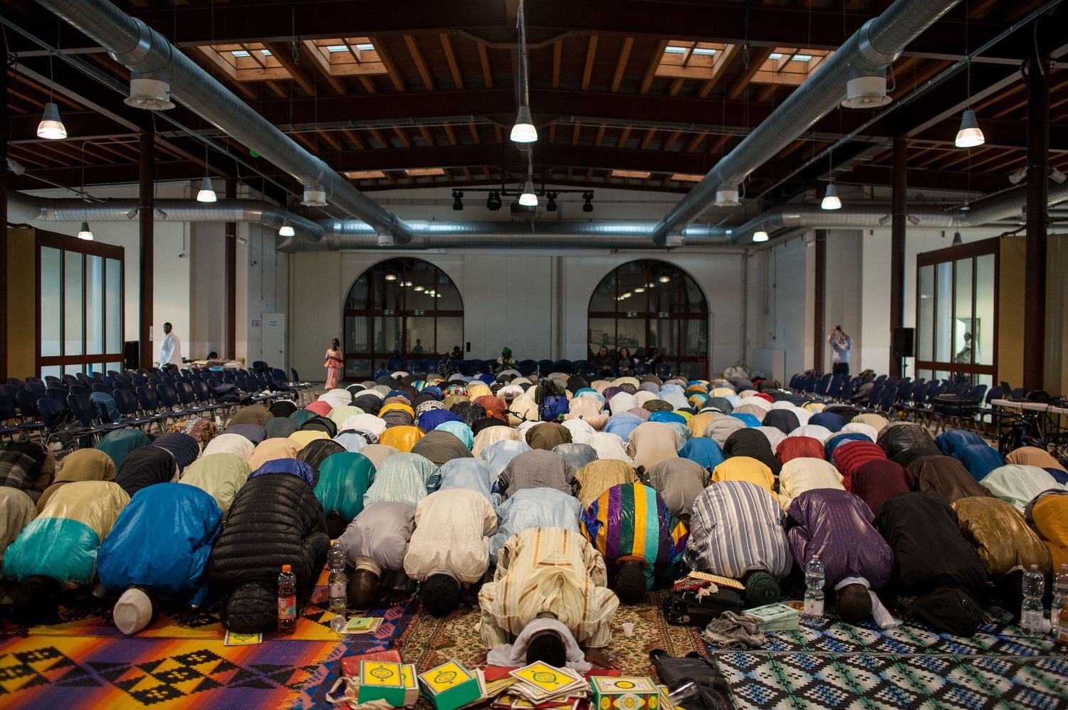 Large congregation of Muslims praying in rows during Friday prayer service inside a spacious mosque hall.
