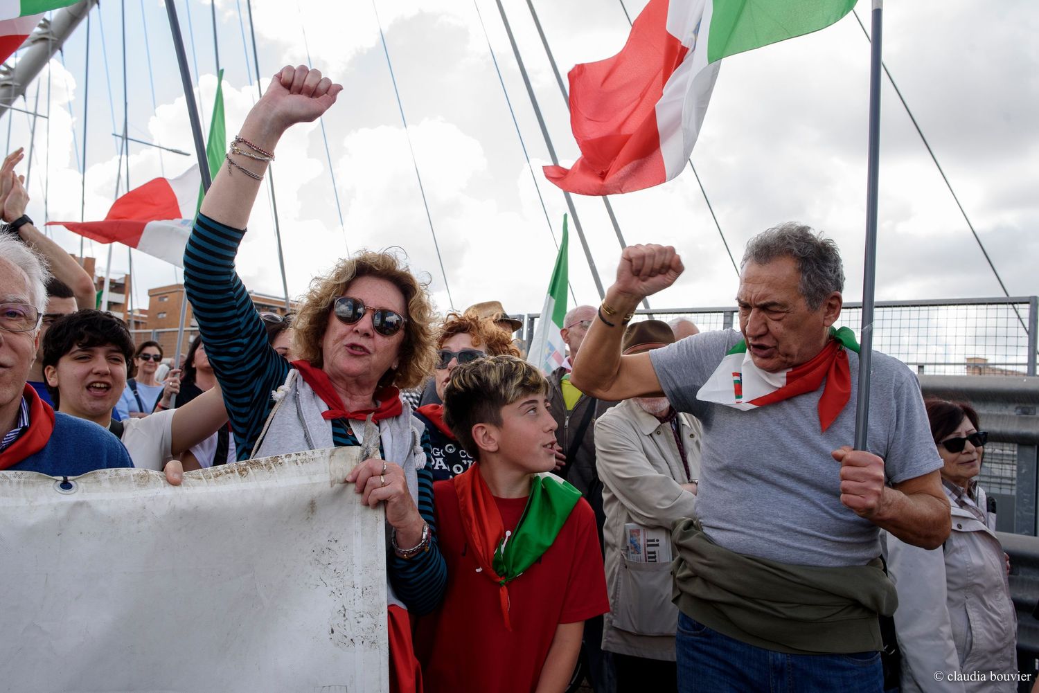 Crowd of Italian protesters raising fists, waving Italian flags at a political rally outdoors.
