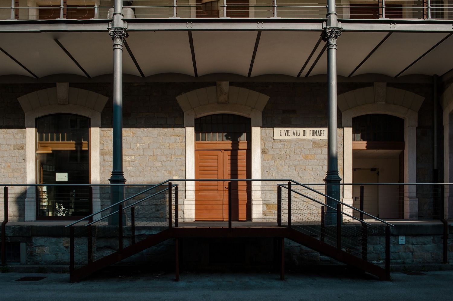 Historic stone building facade with metal columns, wooden door, and accessible ramp entrance in warm sunlight.
