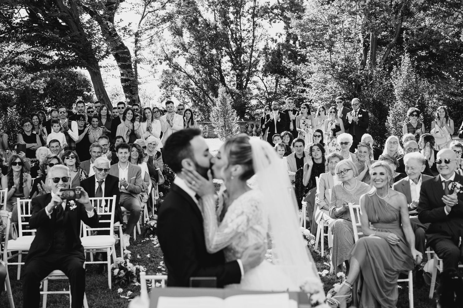 Wedding guests celebrate during an outdoor garden ceremony with white chairs and natural greenery.
