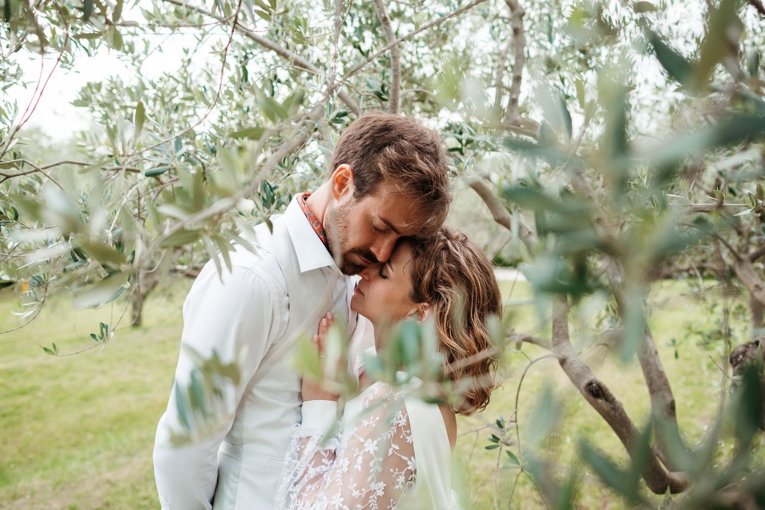 A romantic couple embraces under olive trees in a sun-drenched Mediterranean grove during a photo session.