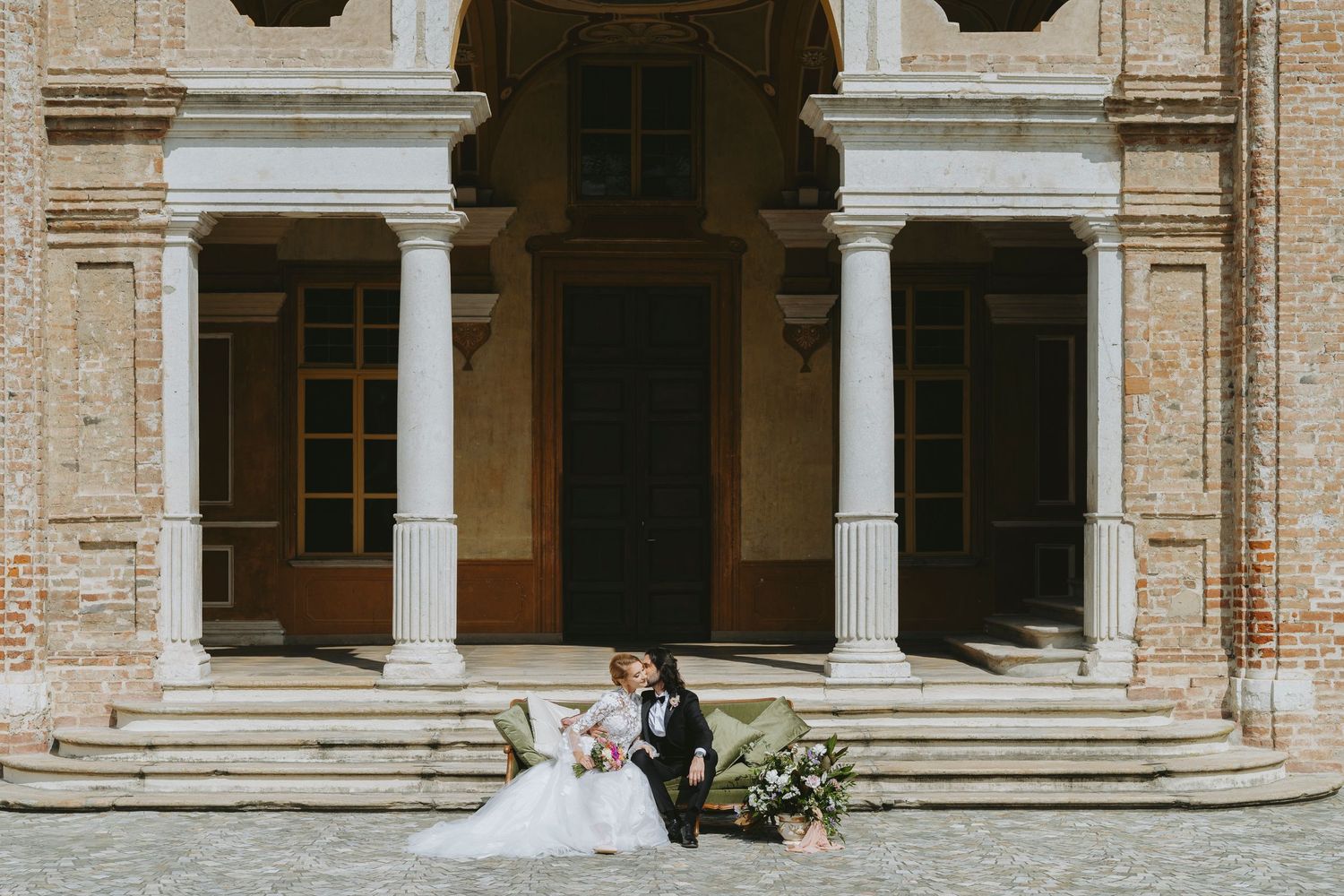 A couple sits together on elegant stone steps of a historic building with classic architectural columns and details.