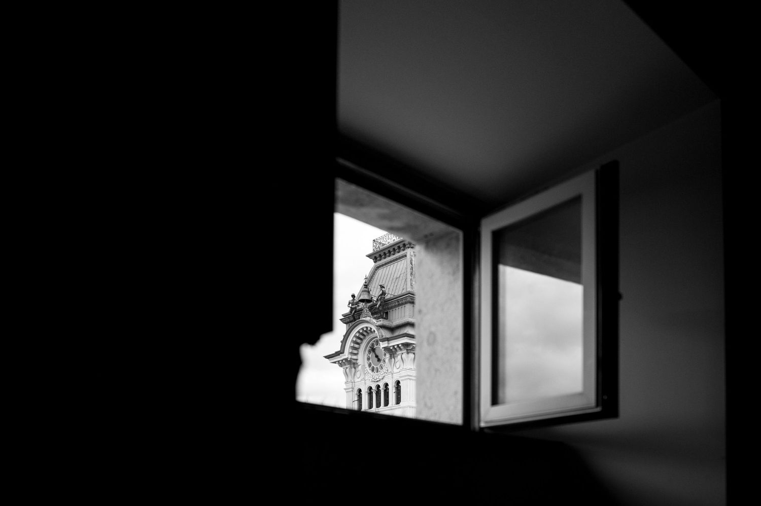 Black and white photo of an open window revealing an ornate building facade in dramatic contrast.