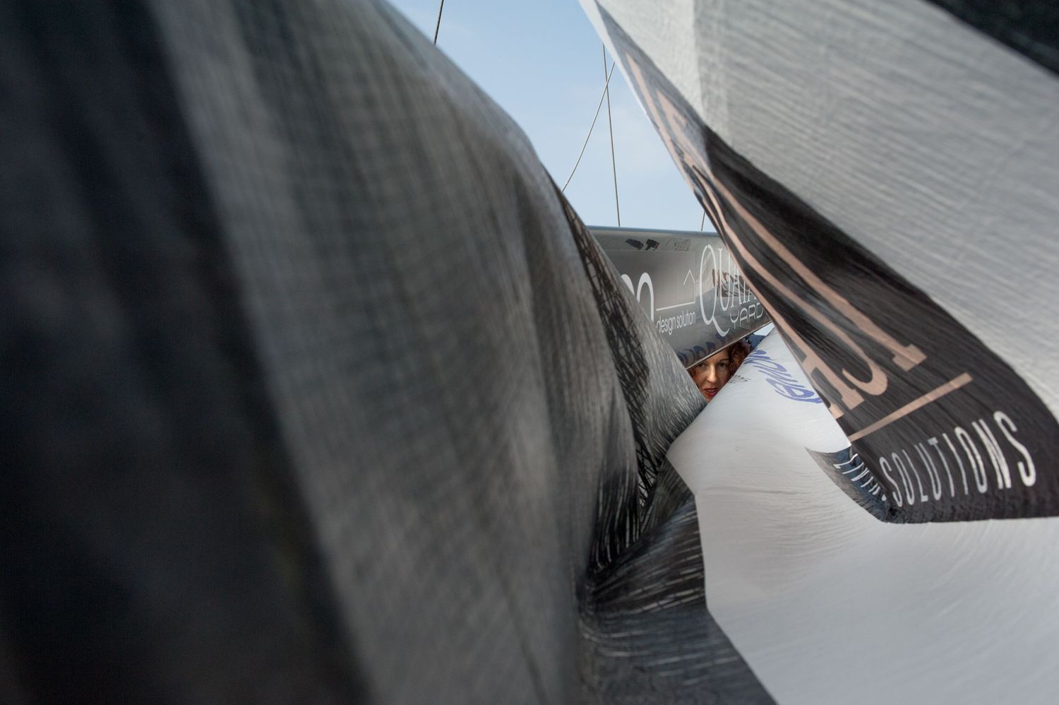 Close-up of large dark carbon fiber sailing boat sails billowing in the wind against a clear blue sky.