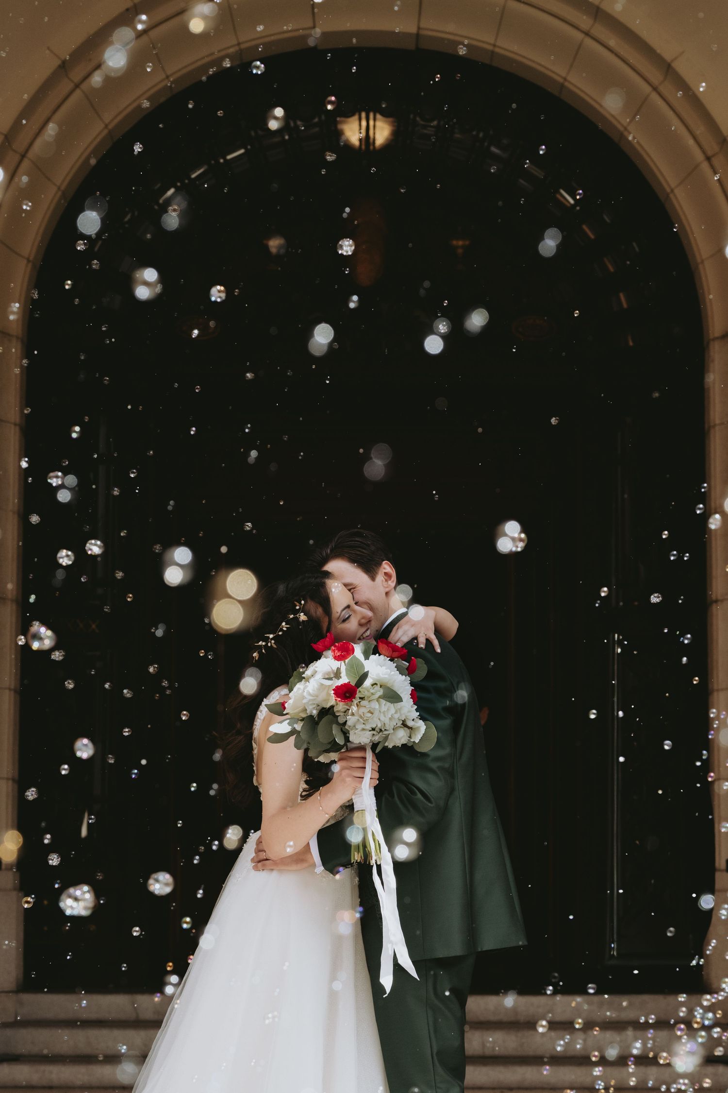 A romantic wedding scene with snow falling while the couple embraces under stone archways.