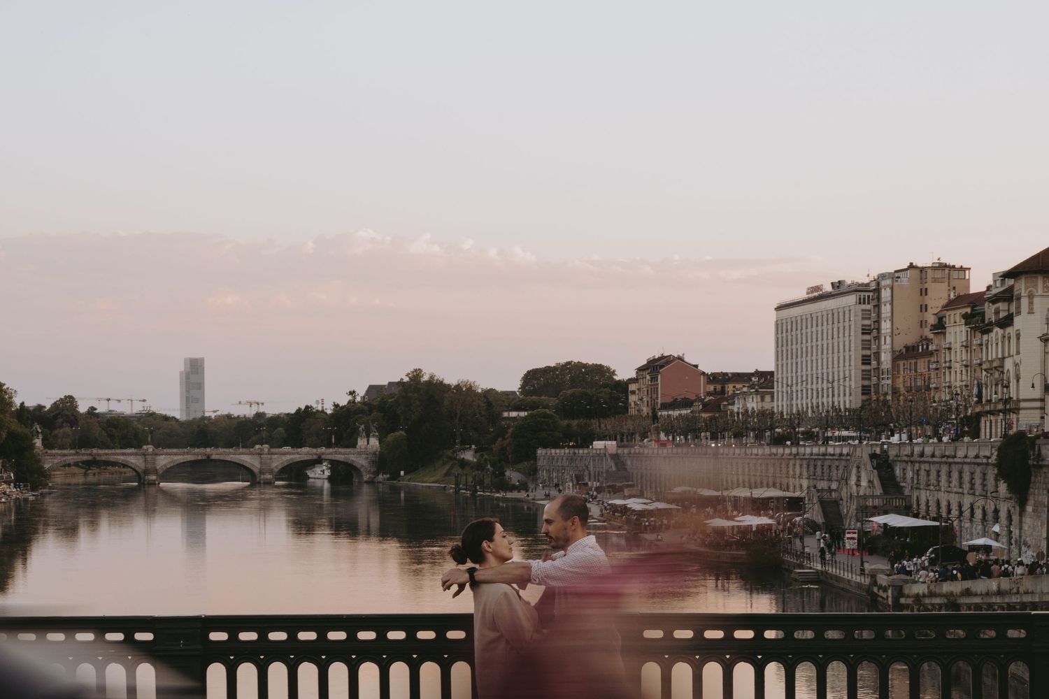 Scenic waterfront cityscape at sunset with a bridge and buildings reflecting on calm waters.
