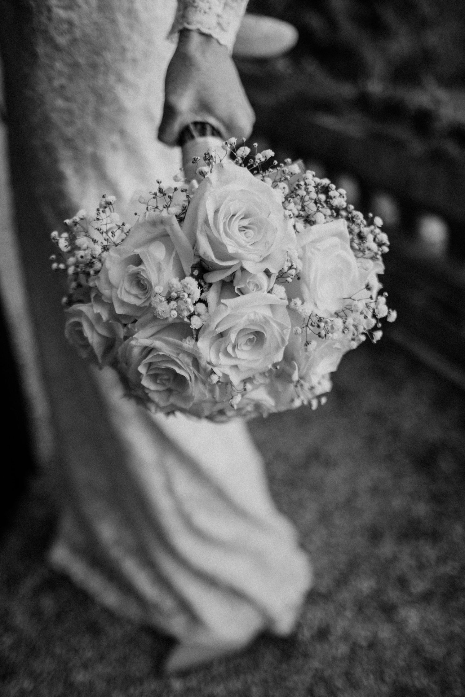 Black and white photo of a bride holding a elegant wedding bouquet of roses and baby's breath.