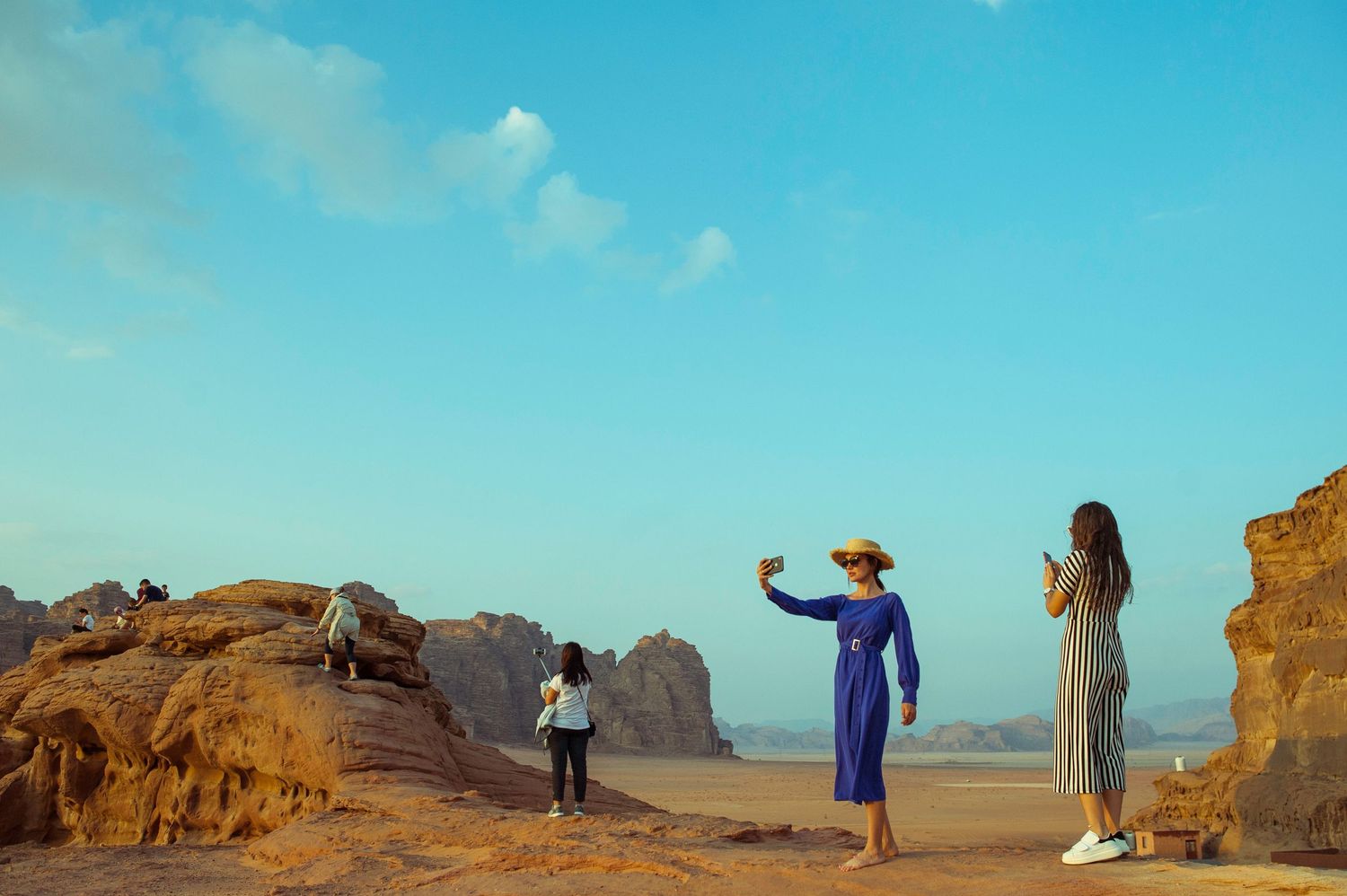 Tourists taking photos in Wadi Rum desert, Jordan, with red sandstone rock formations under a clear blue sky.