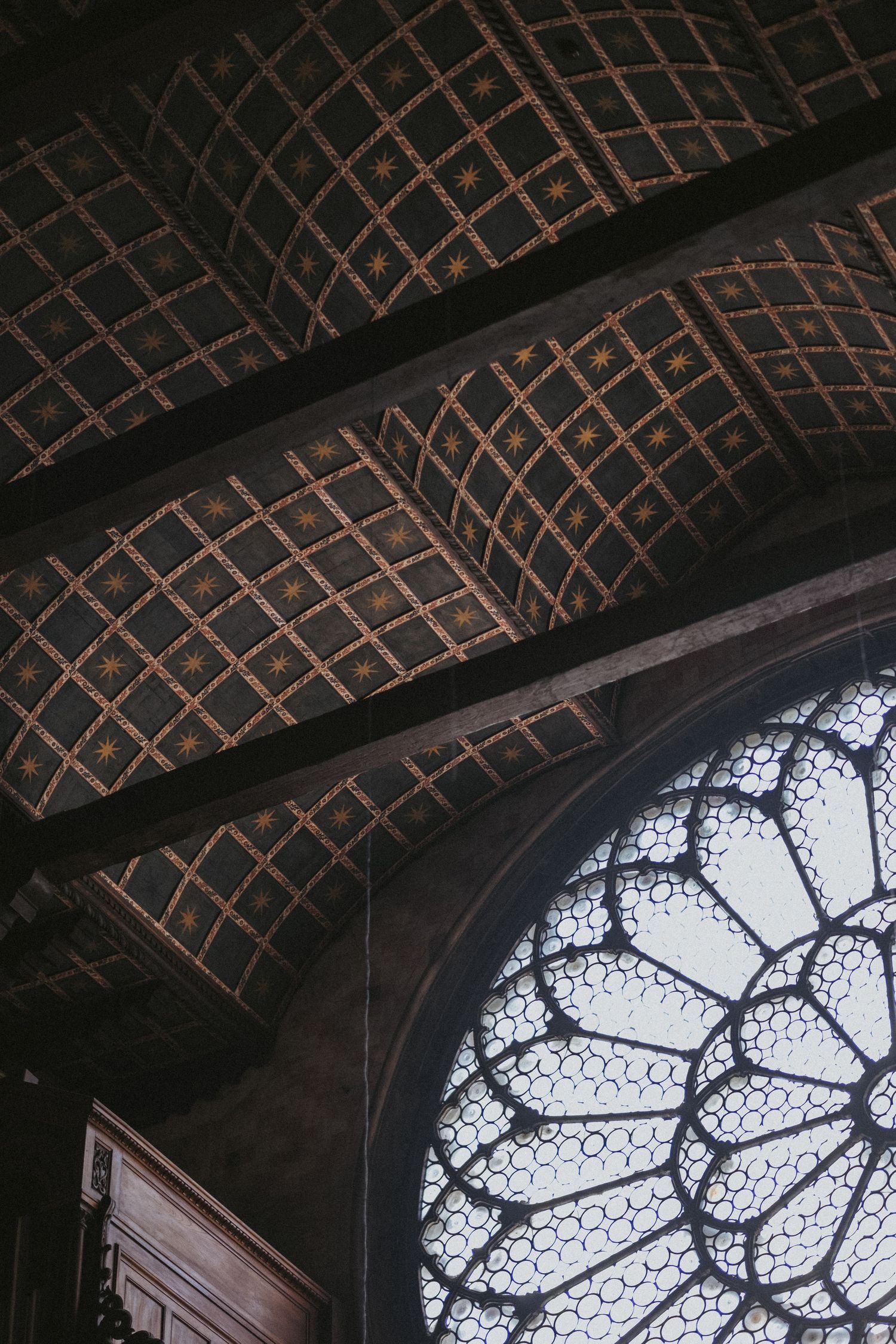 Gothic cathedral ceiling with ornate gold star patterns and a large circular rose window with intricate stone tracery.