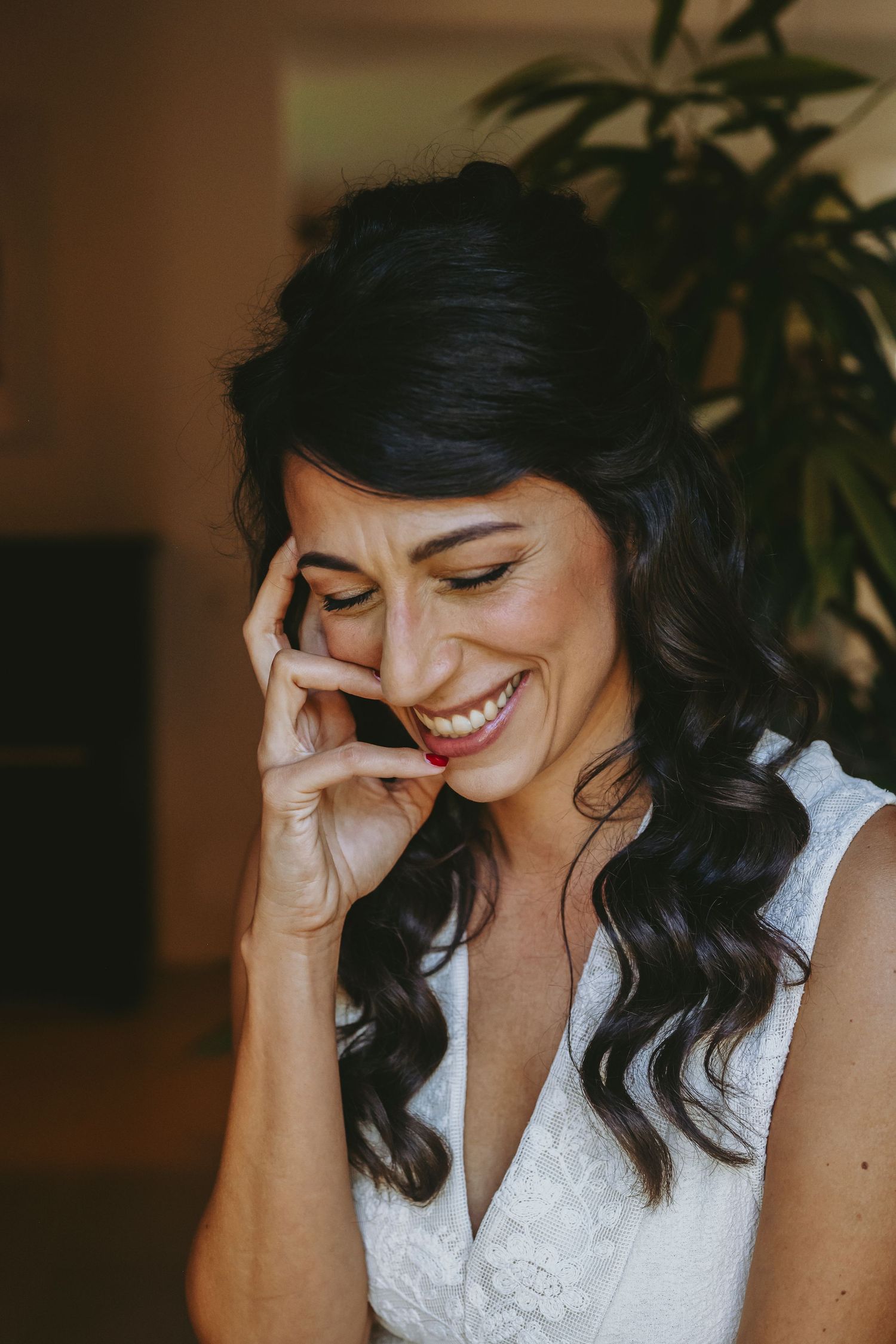 A joyful moment captured in warm lighting as someone laughs with eyes closed while wearing a white lace dress.