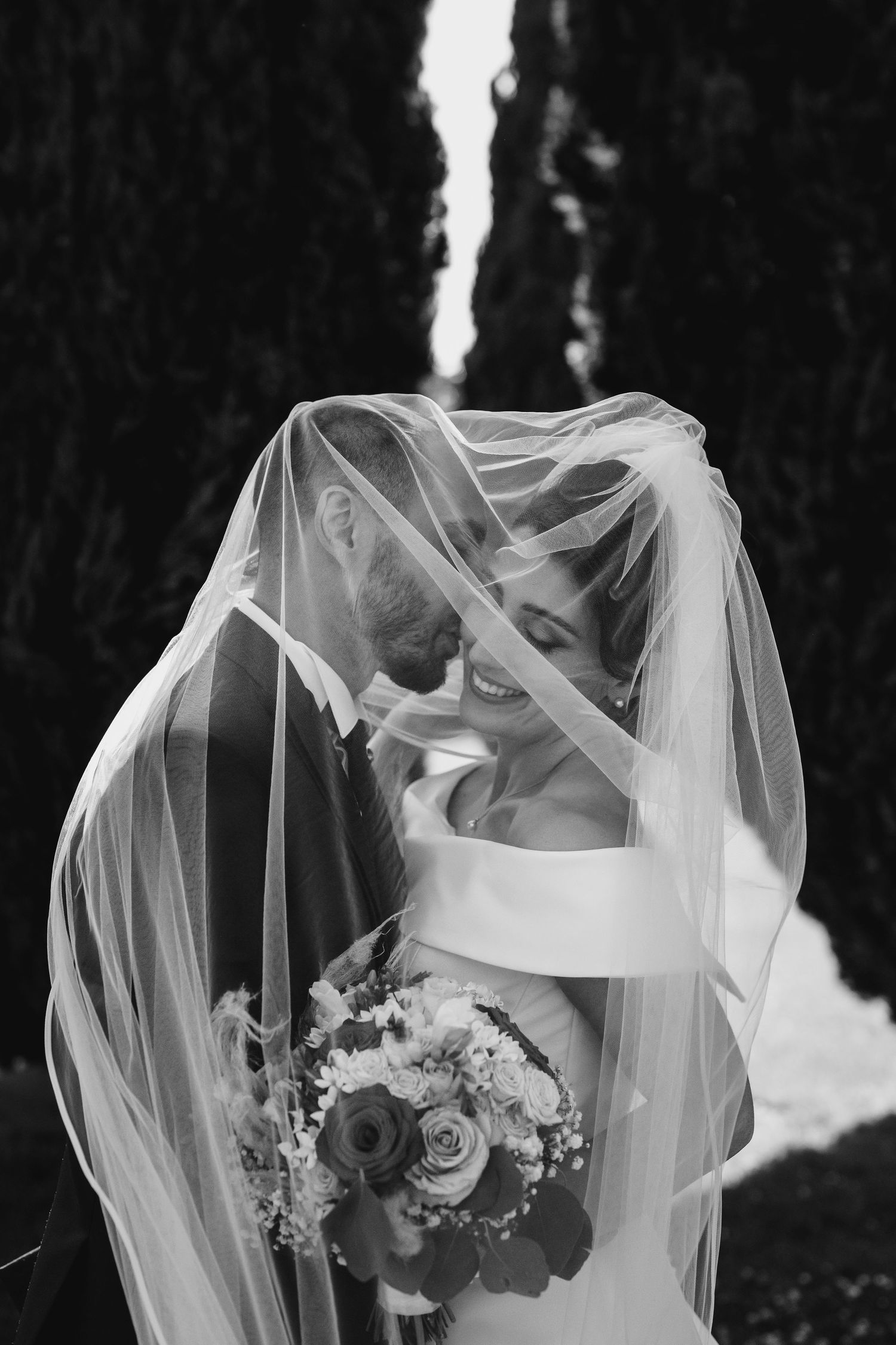 A romantic black and white wedding photo with a couple embracing under a flowing veil..